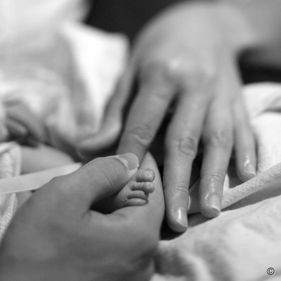 Klein baby voetje tussen handen ouders