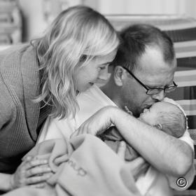 Baby in armen vader moeder kijkt over schouder vader mee